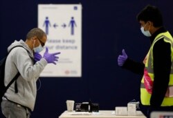 A London Underground worker, right, hands over a free face mask, gloves and hand sanitizer to a passenger at London's Baker Street station, June 9, 2020.