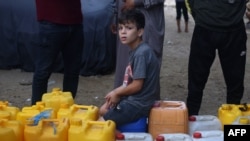 Mladi Palestinac sjedi na plastičnim kanistrima na mjestu za punjenje vode u Rafahu u južnom pojasu Gaze 28. listopada 2023., usred tekućih borbi između Izraela i palestinske skupine Hamas.