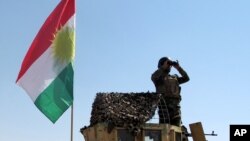 FILE - A member of the Kurdish security forces scans the horizon in Kirkuk, Iraq, from atop a military vehicle flying a flag of the Kurdistan Regional Government, June 14, 2014.