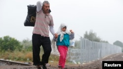 Migrants walk along a railway track as they cross the Hungarian border with Serbia near a collection point in Roszke, Hungary, Sept. 11, 2015.
