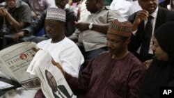 Family members look at a photograph published in a newspaper of Shehu Sahad, who died in a plane crash, as they wait to identified his body in Lagos, Nigeria, June 5, 2012.