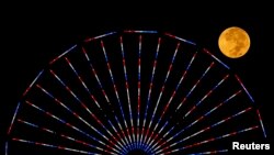 FILE - The moon is pictured behind a Ferris wheel on the pier in Santa Monica, California, after a total lunar eclipse, also known as a "blood moon," Oct. 8, 2014. A total lunar eclipse unfolds again the night of May 15, 2022, and into the morning of May 16.