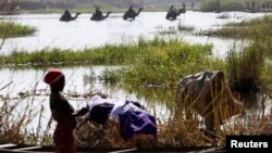 FILE - Men on camels cross the water as a woman washes clothes in Lake Chad at Ngouboua.