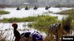 FILE - Nigerians fleeing Boko Haram attacks continue to enter Chad; men on camels cross the water as a woman washes clothes in Lake Chad at Ngouboua, Jan. 19, 2015.
