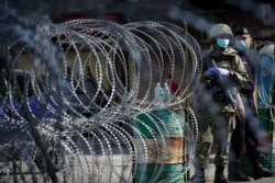 FILE - A soldier and a policeman wearing face masks stand guard near barbed wire in a locked down area due to the new coronavirus in Kuala Lumpur, Malaysia, May 15, 2020.