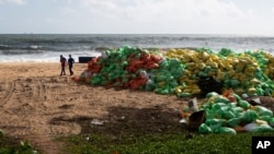 Sri Lankans walk past a pile of plastic pellets washed ashore from the fire damaged container ship MV X-Press Pearl at Kapungoda, on the outskirts of Colombo, Sri Lanka, Friday, June 11, 2021. Sri Lankan authorities say they have taken water samples…