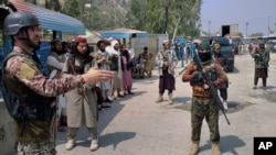 A Pakistani paramilitary soldier, left, and Taliban fighters stand guard on their respective sides, at a border crossing point between Pakistan and Afghanistan, in Torkham, in Khyber district, Pakistan, Sept. 5, 2021.