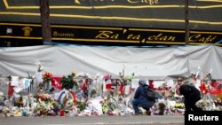 People mourn in front of the screened-off facade of the Bataclan Cafe adjoining the concert hall, one of the sites of the deadly attacks in Paris, France, a day before a ceremony to pay tribute to the 130 victims, Nov. 26, 2015. 