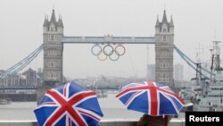 Two tourists stand under Union flag umbrellas as they take pictures from London Bridge, of Tower Bridge adorned with the Olympic rings, on a wet summer's morning in central London July 6, 2012.