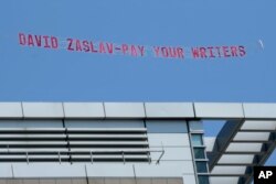 A message in support of the Hollywood writers' strike is pulled by an airplane in the sky above Boston University commencement ceremonies, Sunday, May 21, 2023, in Boston, during an address by David Zaslav, president and CEO of Warner Bros. Discovery. (AP Photo/Steven Senne)