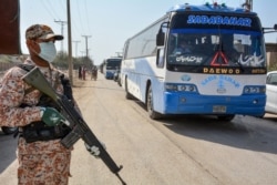 A soldier wearing a face mask stands guard as buses carry pilgrims returning from Iran via the Pakistan-Iran border town of Taftan, leading to a quarantine facility zone to prevent the spread the COVID-19, in Sukkur in Sindh province, March 18, 2020.