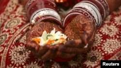 Seorang pengantin wanita memegang bunga dengan tangannya yang dihiasi dengan pasta pacar selama upacara pernikahannya di kota Ahmedabad, India barat. (Foto: Reuters)