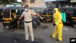 A civic worker sprays disinfectant on a policeman standing guard after a protest by migrant workers against the extension of the lockdown, in a slum in Mumbai, India, April 14, 2020. 