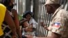 A Haitian police officer asks a woman to move away from a gate at the US Embassy in Port-au-Prince, Haiti, July 9, 2021.