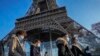 Para pengunjung mengenakan masker untuk melindungi dari penularan COVID-19, melintas di depan Menara Eiffel di Paris, Perancis, 21 Desember 2021. (Foto: Michel Euler/AP Photo)