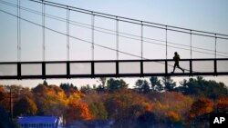 A jogger crosses the Swinging Bridge over the Androscoggin River on a frosty autumn morning, Nov. 4, 2021, in Brunswick, Maine. 