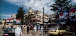 FILE - In this March 24, 2020 file photo, workers spray disinfectant to prevent the spread of the coronavirus, on a street lined with billboards showing Syrian President Bashar Assad, in Qamishli, Syria.