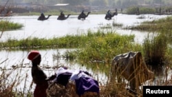 FILE - Men on camels cross the water as a woman washes clothes in Lake Chad in Ngouboua, Jan. 19, 2015