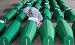 FILE - A girl inspects coffins prepared for burial in Potocari near Srebrenica, Bosnia. The remains of 33 victims of Srebrenica massacre will be buried July 11, 2019, 24 years after Serb troops executed some 8,000 Muslim men and boys.