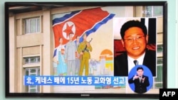 Passersby watch a local television broadcast in Seoul on May 2, 2013 showing a report and picture of Kenneth Bae (R), a Korean-American tour operator detained in North Korea, against the background of a North Korean flag painted on the wall of a building 