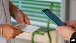 FILE - A teacher, left, has his "green pass" checked by a school worker as he arrives at the Isacco Newton high school, in Rome, Italy, Sept. 13, 2021. 