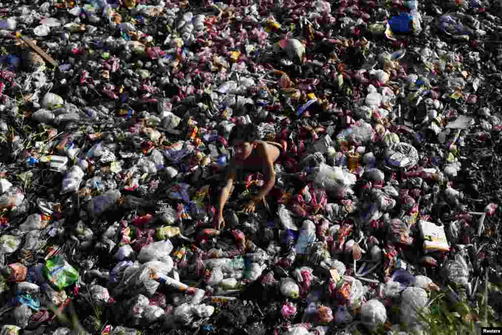 Seorang anak laki-laki mengumpulkan barang-barang plastik bekas dari tumpukan sampah di daerah pembuangan utama di Lahore, Pakistan.