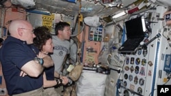 Astronauts Scott Kelly, left, Expedition 26 commander; Cady Coleman, center, Expedition 26 flight engineer; and Michael Barratt, STS-133 mission specialist, watch a monitor in the International Space Station while space shuttle Discovery remains docked wi