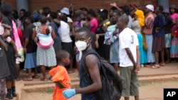 A man wearing a mask is seen near a food queue in Harare, Zimbabwe, March 25, 2020. 