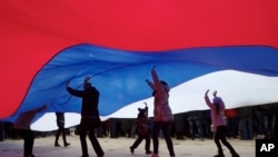 FILE - People stand under the giant national flag during the Vesna (Spring) festival commemorating the annexation, in Moscow, Russia, March 18, 2017.