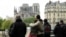 FILE - People hug while looking at Notre-Dame-de-Paris in the aftermath of a fire that devastated the cathedral, April 16, 2019. 