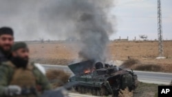Syrian opposition fighters drive past a burning government armored vehicle south of Hama, Syria, on Dec. 7, 2024.