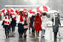FILE - Women wearing carnival masks march down the streets under umbrellas with the colors of the former white-red-white flag of Belarus to protest against the Belarus presidential election results in Minsk, on Jan. 26, 2021.