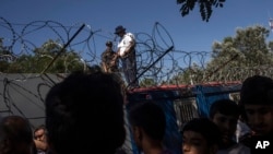 FILE - Hungarian police and army officers oversee the distribution of food as people queue at a camp in Horgos, Serbia, on Serbia's border with Hungary, July 11, 2016. 