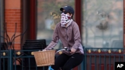 A bicyclist wears face protection against the new coronavirus while pedaling through Larimer Square early Saturday, April 25, 2020, in downtown Denver.