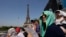 FILE - Stephanie Touissaint, foreground, uses a fan to keep cool in the sweltering heat at Eiffel Tower Stadium during a beach volleyball match between Cuba and Brazil at the 2024 Summer Olympics in Paris, July 30, 2024.