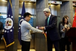 FILE - IBM employee Yang Bo shakes hands with then-U.S. Secretary of State John Kerry after being the first Chinese citizen to be issued a 10-year visa, at the U.S. Embassy in Beijing, Nov. 12, 2014.