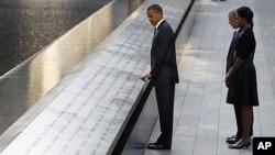 President Barack Obama touches the names of victims engraved on the side of the north pool of the World Trade Center site as former President George W. Bush, first lady Michelle Obama and former first lady Laura Bush (obscured) look on during ceremonies m