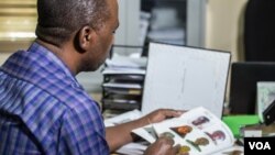 Edward Muthoka of the ICRC leafs through a photo book of registered missing persons, in Maiduguri, Nigeria. (C. Oduah/VOA)