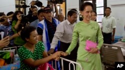 Myanmar's opposition leader Aung San Suu Kyi, center, greets a patient in a bed at Yangon General Hospital in Yangon, Myanmar, Oct. 30, 2015. 