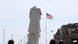 FILE - Passers-by walk near a damaged Christopher Columbus statue, Wednesday, June 10, 2020, in a waterfront park near the city's traditionally Italian North End neighborhood, in Boston.
