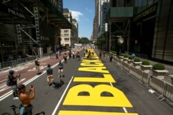 FILE - Volunteers and members of the media walk along a Black Lives Matter sign that was painted on Fifth Avenue in front of Trump Tower, in New York, July 9, 2020.