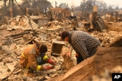 Robert Lara, left, looks for belongings along with his stepfather after the Eaton Fire burns in Altadena, California, Jan. 9, 2025.