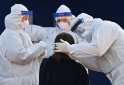A medical staff member wearing protective gear takes a swab from a woman to test for the COVID-19 coronavirus at a temporary testing station outside Seoul station in Seoul, Dec. 14, 2020.
