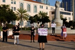 Social Worker Iris Trammel (C) hold a sign during a vigil to honor San Diego county employees who have lost their lives to the coronavirus (COVID-19) while working the frontline of the pandemic in San Diego, California, Aug. 24, 2020.