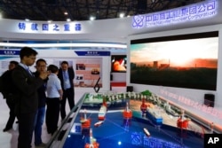 FILE - Staff members from the China National Nuclear Corporation look at models of oil tanker-shaped floating nuclear reactors and oil rigs showcased at the display booth of China's state-owned CNNC, in Beijing, April 27, 2017.