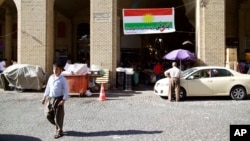 FILE - A man walks past a campaign slogan printed on a Kurdish flag urging people to vote "yes" in the upcoming poll on independence from Iraq, in Irbil, Iraq, Aug. 24, 2017.