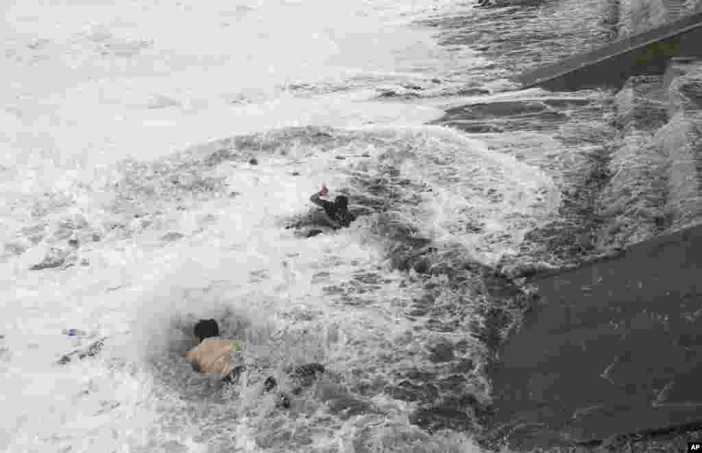 A man jumps into the water to rescue a woman who fell due to strong tidal waves on the Bay of Bengal coast at Gopalpur, Orissa, Oct. 12, 2014.