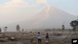 Villagers stand on an area covered in volcanic ash as Mount Semeru looms in the background in Kajar Kuning village in Lumajang, East Java, Indonesia, Monday, Dec. 5, 2022. 