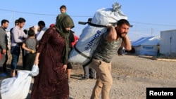 Familias sirias desplazadas, que huyen de la violencia después de la ofensiva turca en Siria, reciben ayuda en el campamento de refugiados de Bardarash en las afueras de Dohuk, Irak, el martes, 22 de octubre, de 2019.