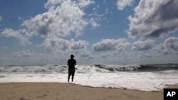 A beachgoer stands at the edge of the water, Sunday, Sept. 4, 2016, in Bridgehampton, N.Y., on the southeastern shore of Long Island, where the effects of storm system Hermine could be seen in the rough surf and a ban on swimming. 